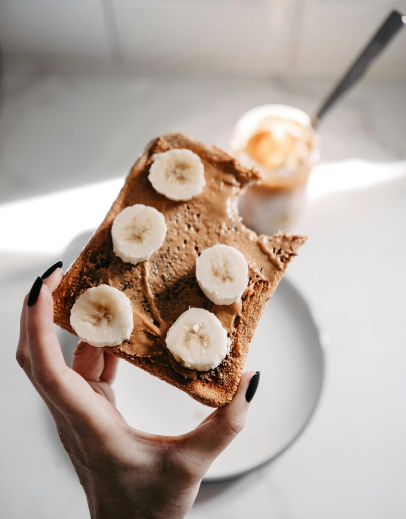 A close-up of a hand holding a peanut butter and banana toast, ideal for breakfast or snack.